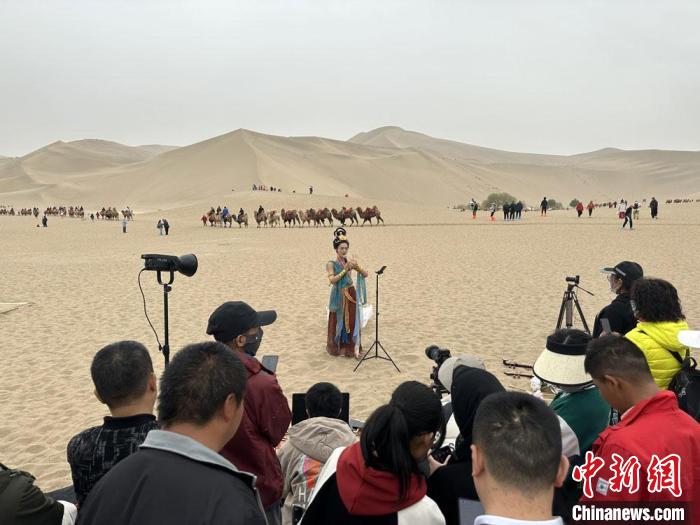 圖為2023年4月底，敦煌大漠“逐舞者”奧楠在鳴沙山月牙泉景區(qū)視頻直播，吸引游人圍觀?！●T志軍 攝